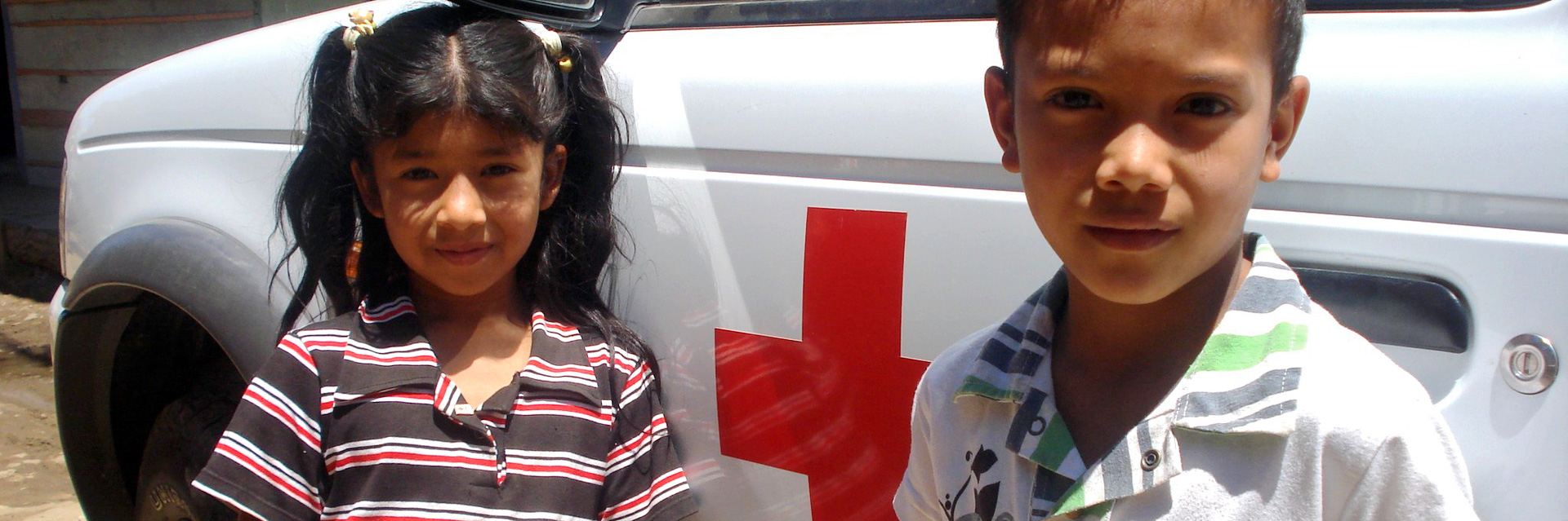 Foto: Ein Mädchen und ein Junge in Kolumbien vor einem Rotkreuz-Fahrzeug