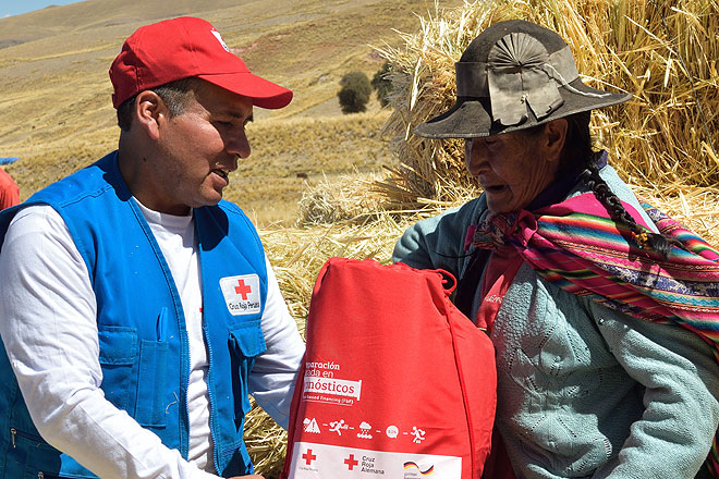 Ein Mitarbeiter des peruanischen Roten Kreuzes übergibt ein Hilfspaket an eine Alpaka-Züchterin in Peru.