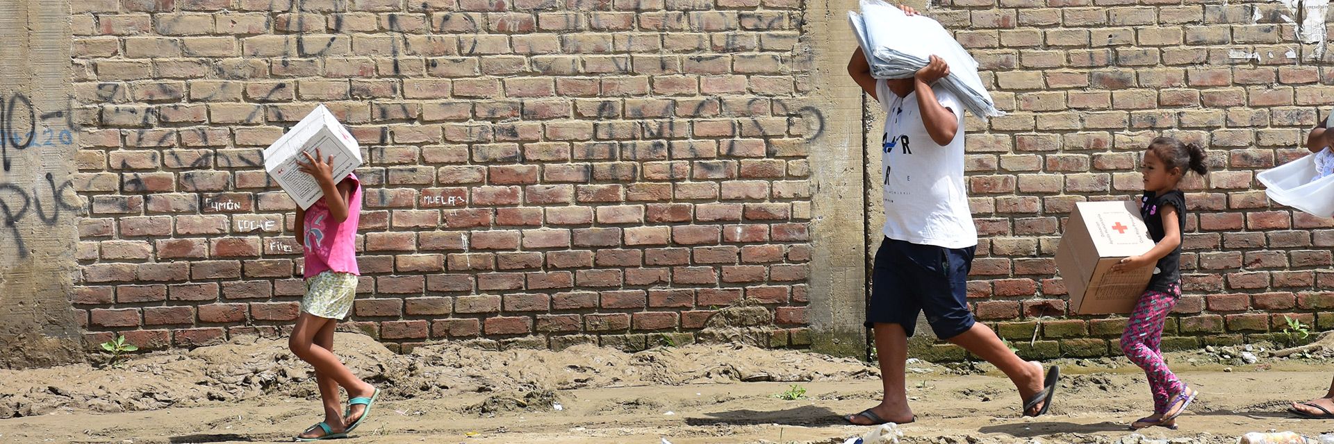 Peruanische Kinder tragen Hilfsgüter vor einer Mauer