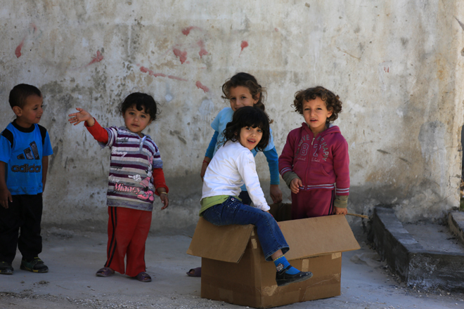 Foto: syrische Flüchtlingskinder spielen vor einer grauen Wand mit Pappkarton