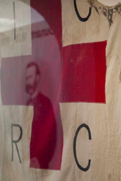 Im Henry-Dunant-Museum im schweizerischen Heiden spiegelt sich sein Porträt in einer Vitrine mit einer zerschlissenen Rotkreuzfahne, die während des Bürgerkriegs in Angola benutzt wurde. (Jörg F. Müller / DRK)