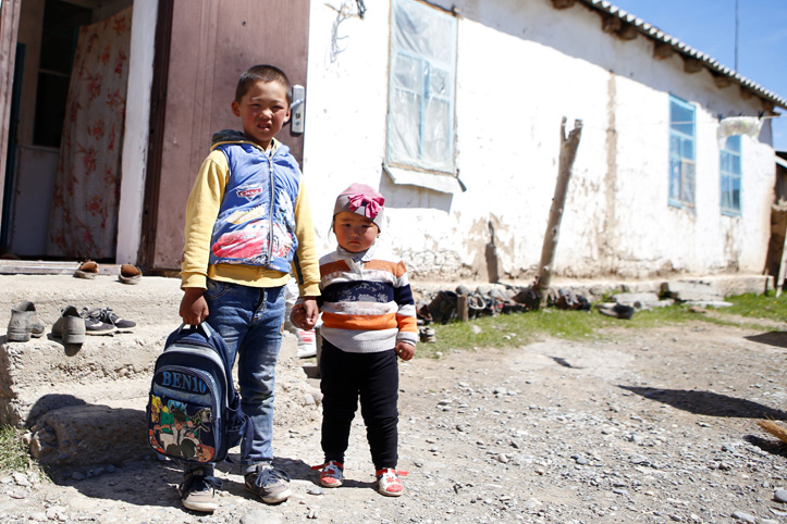 Zwei Kinder mit Rucksack vor marodem Haus