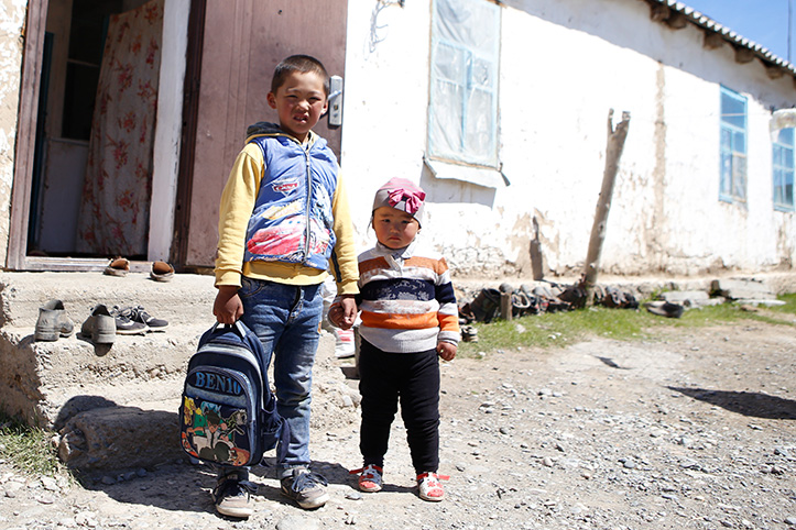 kirgisische Kinder mit Rucksack vor Haus