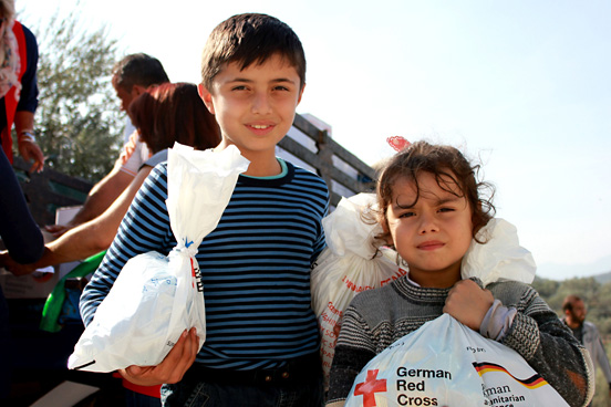 Foto: zwei Flüchtlingskinder mit Hilfsgütern des DRK in der Hand.