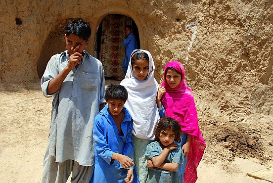 Eine Gruppe von pakistanischen Kindern, zwei Jungen, drei Mädchen, vor einem Höhleneingang im Fels, im Hintergrund einweiteres Kind
