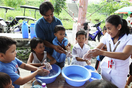 Eine freiwillige Helferin des Philippinischen Roten Kreuzes zeigt Kindern, wie man sich richtig die Hände wäscht.